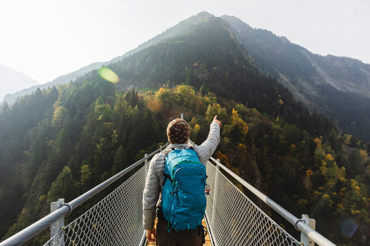 Person steht auf einer Brücke und zeigt mit der Hand auf einen großen Berg der vor ihm zu sehen ist